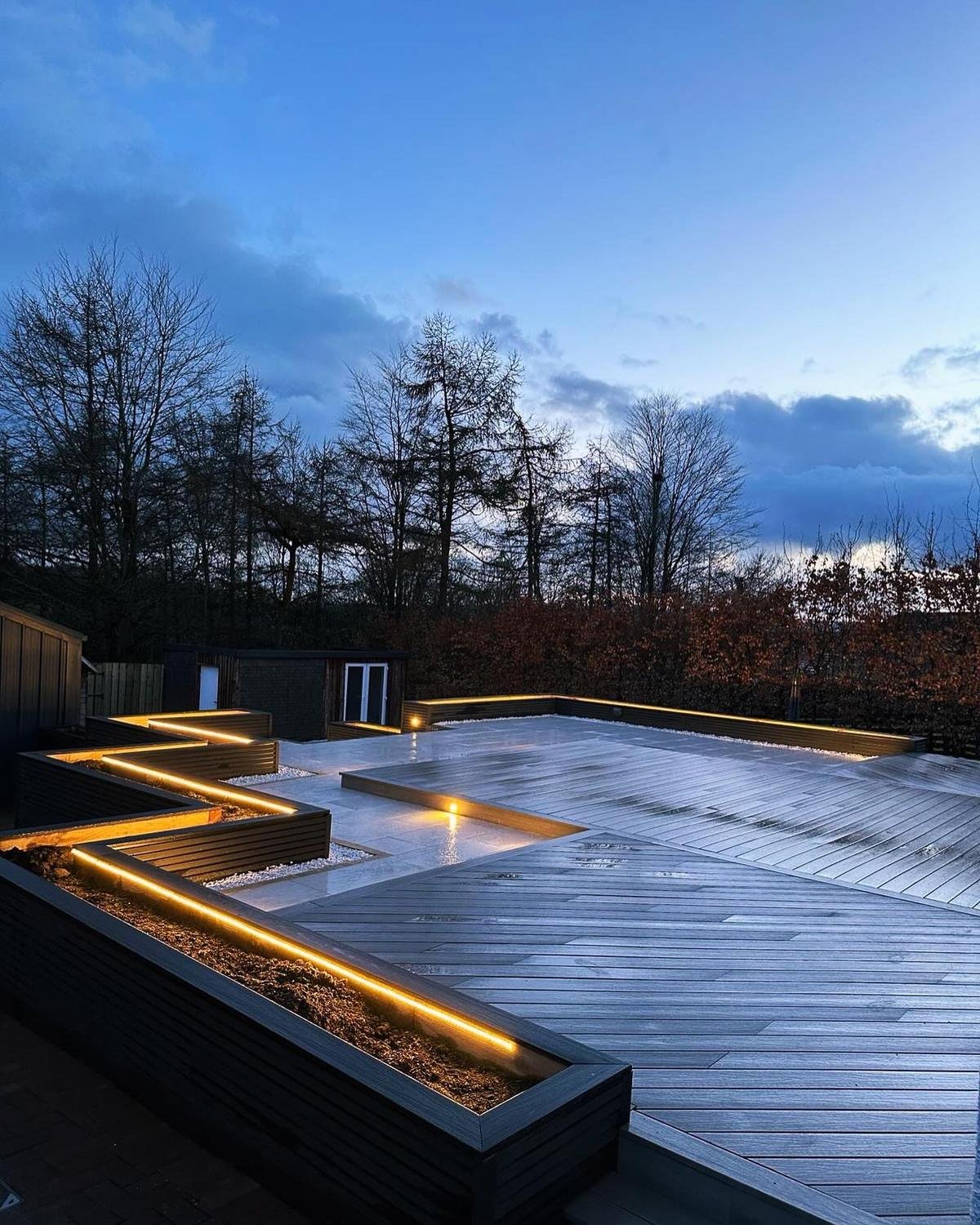 Composite decking at dusk with an angled planter edged in a continuous warm LED strip.