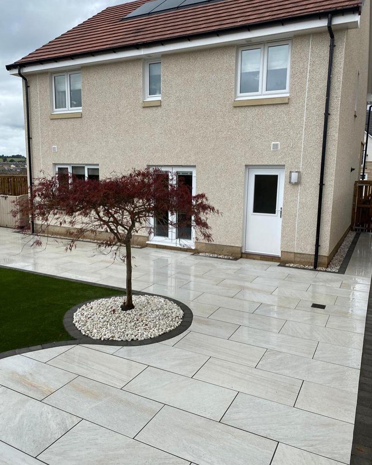 After: the same house with a pale porcelain patio, curved lawn and a red-leaved acer in a ring of white stones.