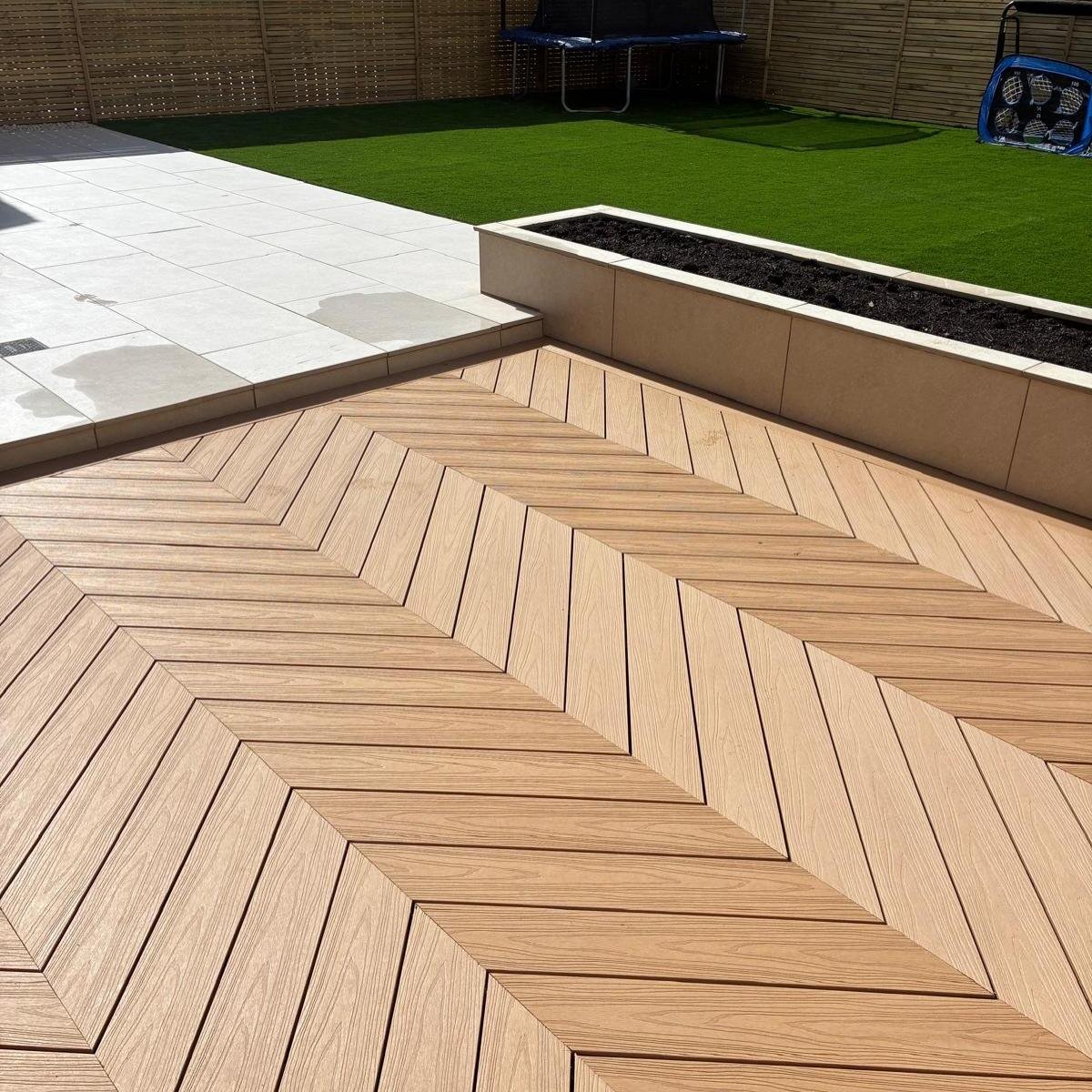 Herringbone decking running alongside a raised rendered planter, with a pale quartz patio and lawn beyond.