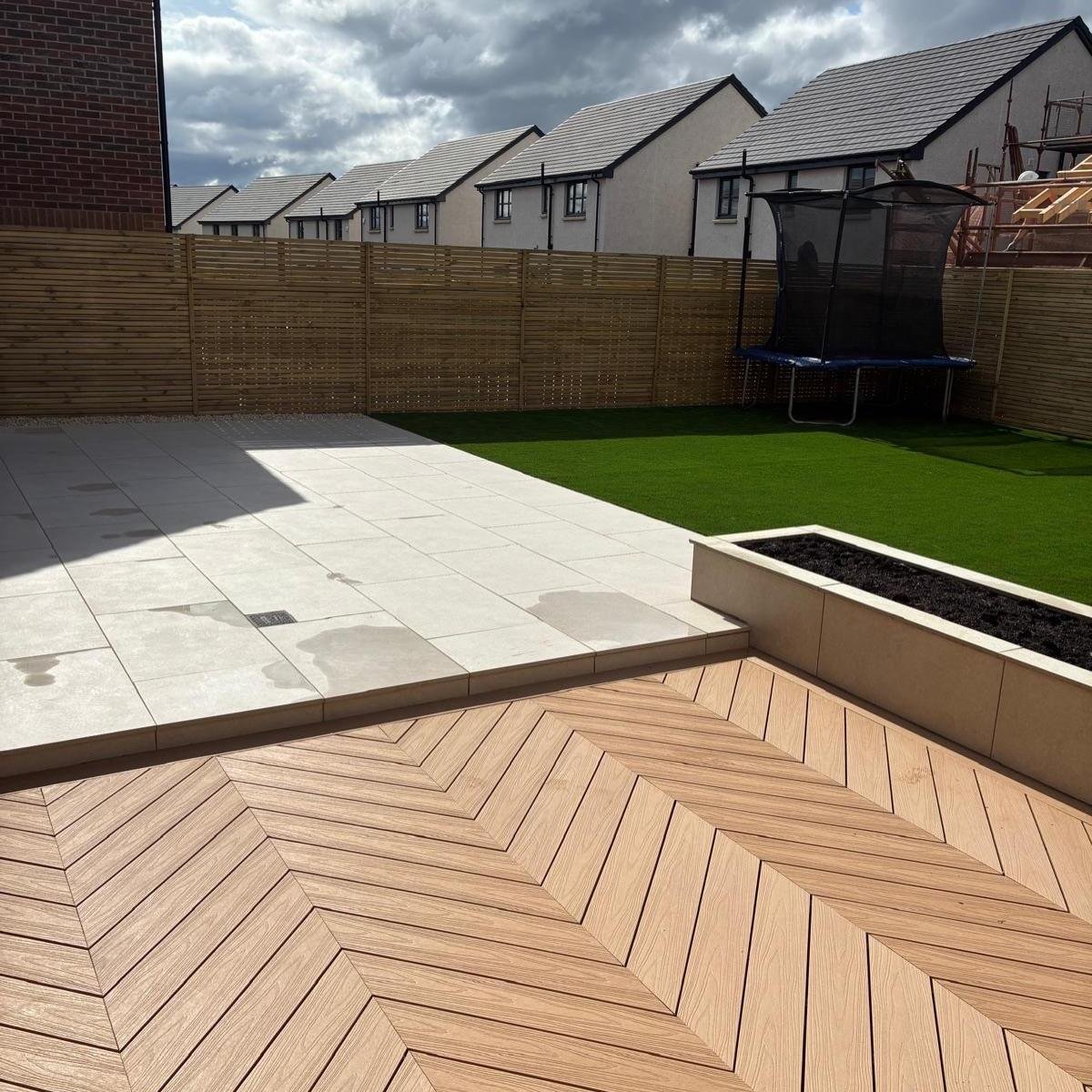 The finished garden: quartz patio stepping down to herringbone decking, planter and synthetic lawn inside new slat fencing.
