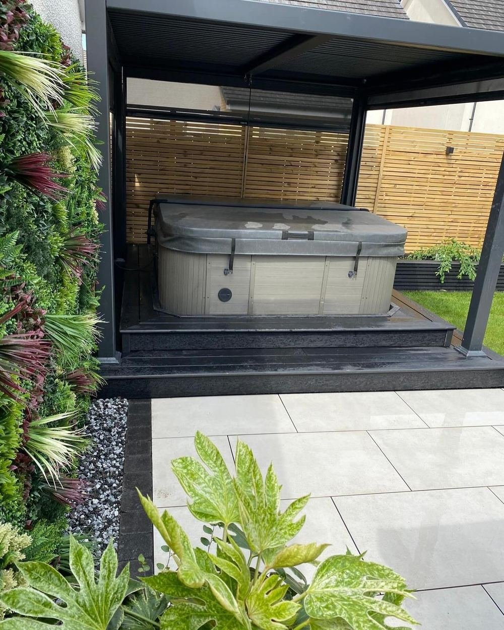Inside the pergola: the hot tub beside the foliage wall, with planting in the foreground.